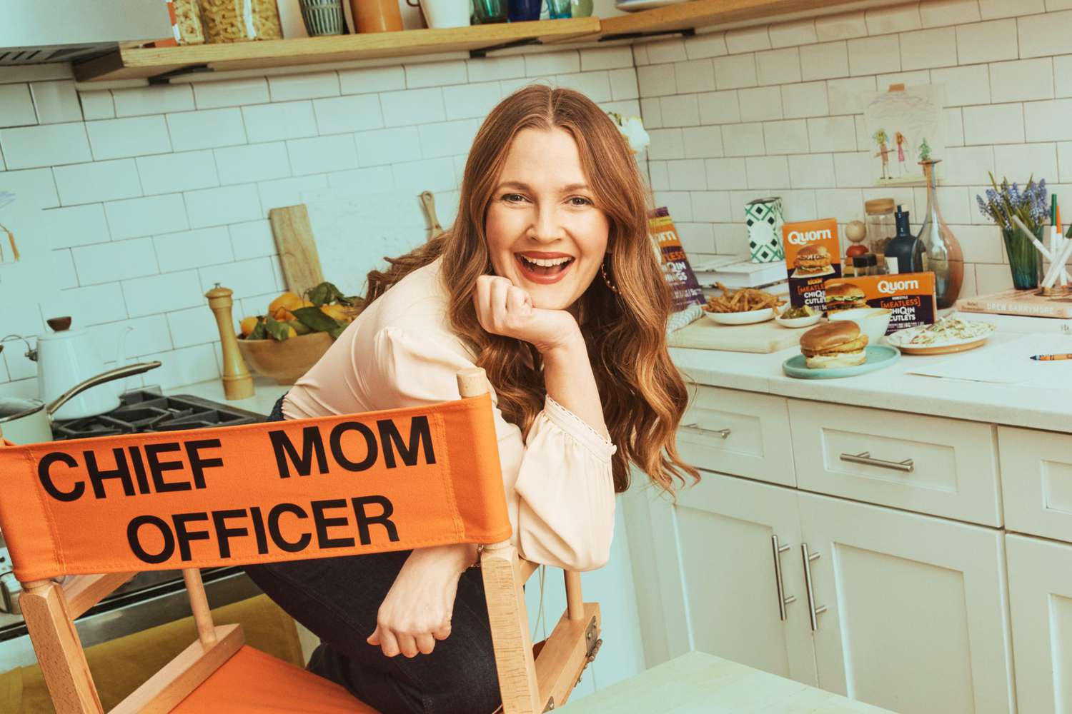 Drew Barrymore sitting in a director's chair in a kitchen
