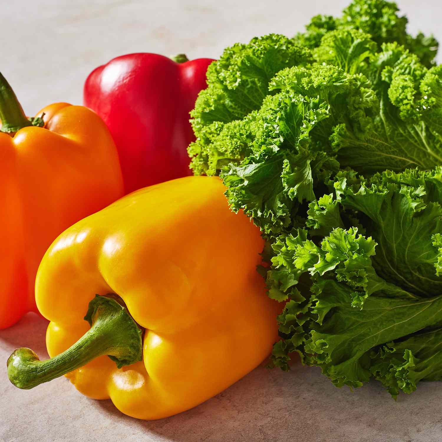 a grouping of red, orange, and yellow peppers with kale