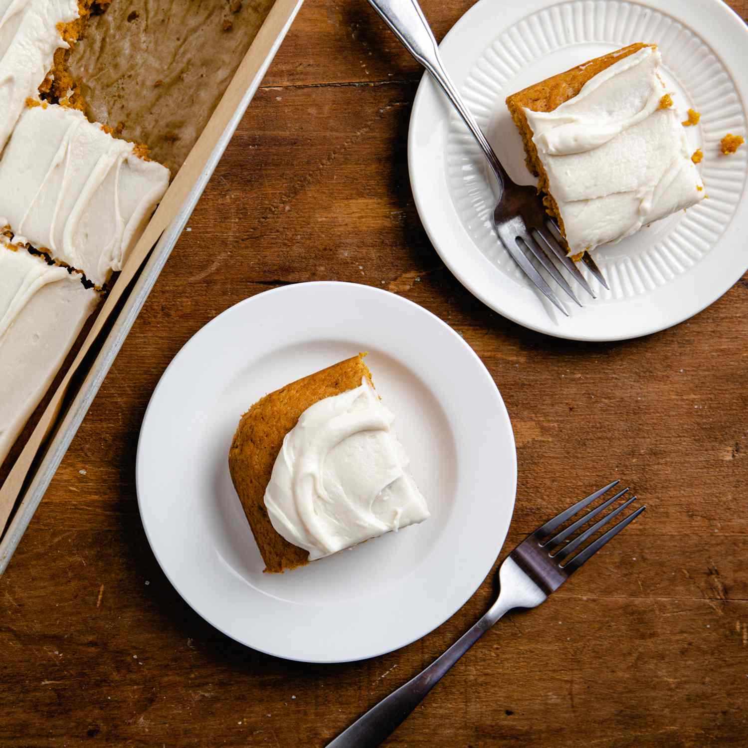 a recipe photo of the Pumpkin Sheet Cake with Cream Cheese Frosting in the cake pan with two slices cut and placed on plates alongside forks