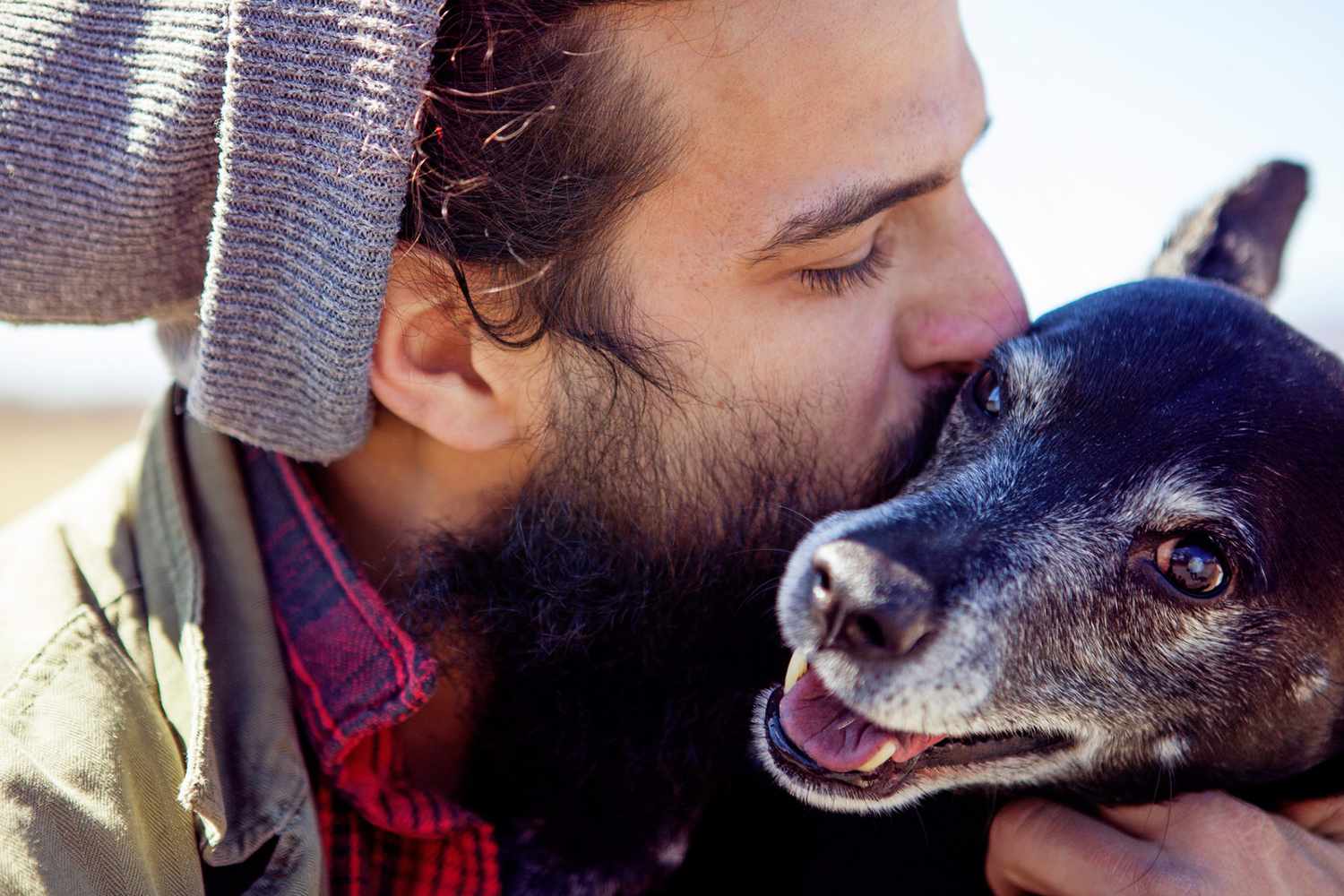 Man with beard kisses black and white dog on the cheek