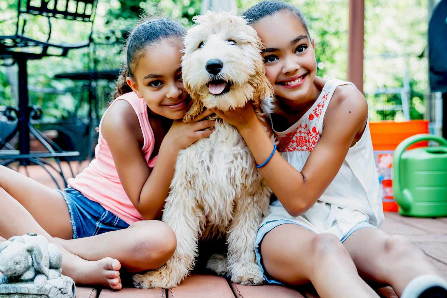 Two girls embrace blond labradoodle from both sides on outdoor deck