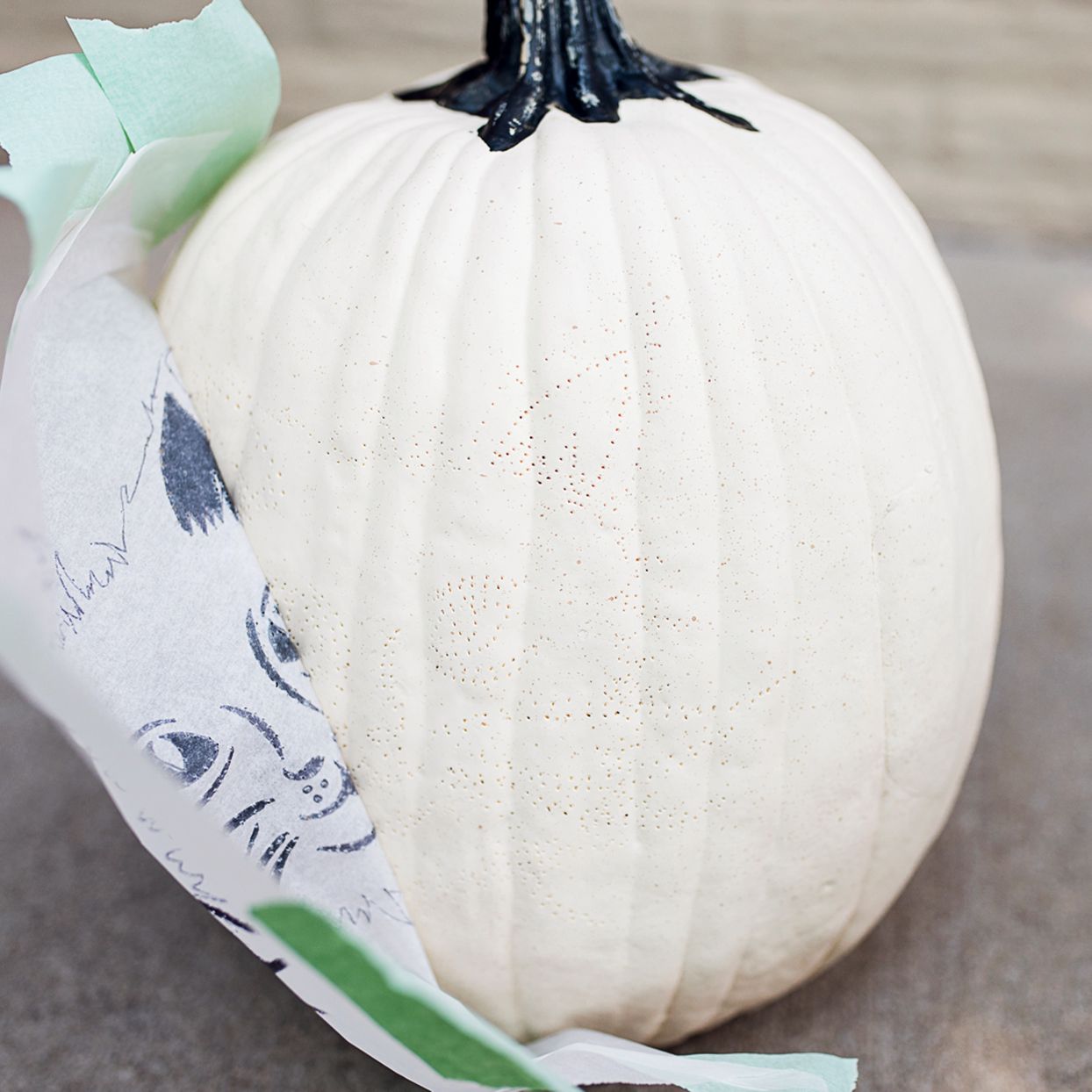 peeling stencil off a white pumpkin with pin points guiding cat pumpkin carving