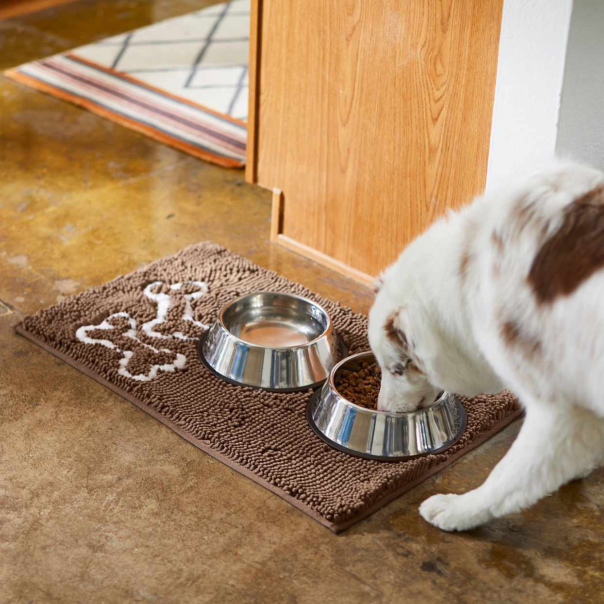 Photo of a dog eating out of a bowl sitting on a Frisco Microfiber Chenille Bones Mat