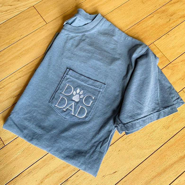 Product photo of a Comfort Colors Dog Dad Tee folded and lying on a wooden surface