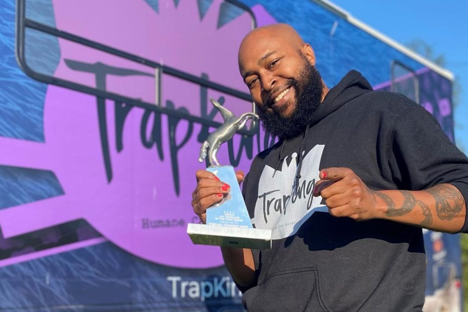 Sterling, the Trapking, holding his award for the 2021 Cat Advocate of the Year Award standing in front of his truck