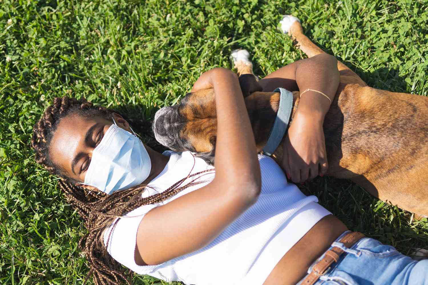 woman lying in grass wearing a face mask hugging her dog