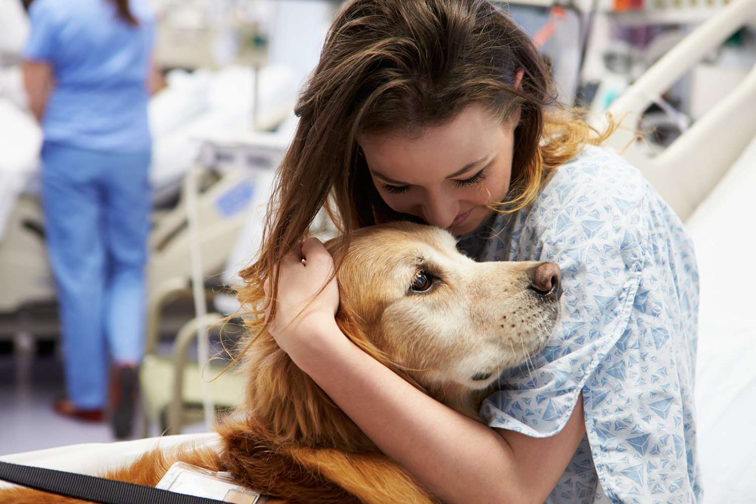 woman in hospital bed hugging a golden retriever therapy dog