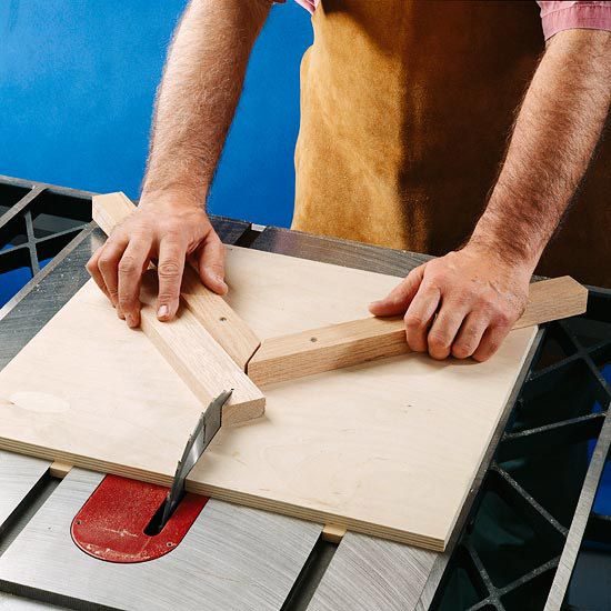 Board on tablesaw with hands holding a type of v shape jig