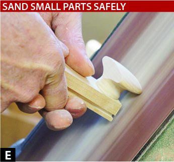 Hands holding a board with a drawer pull glued to it. The drawer pulled is pushed against a sander.