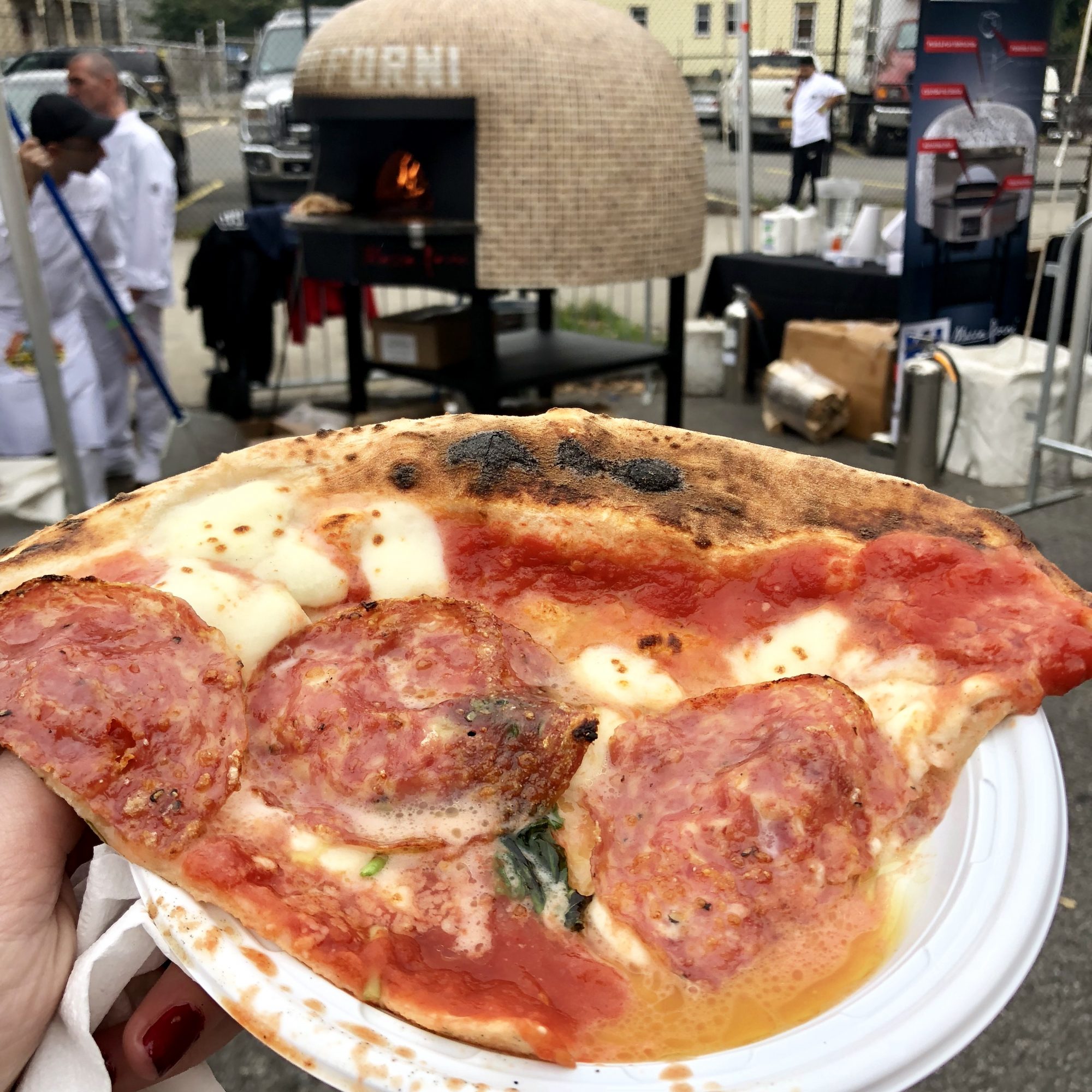 Slice of pizza with pepperoni in front of a portable pizza oven at the 2019 NY Pizza Festival in the Bronx