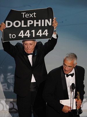 Oscars 2010 | DO IT FOR THE DOLPHINS! On stage with the cast and crew of Best Doc winner The Cove , dolphin trainer Ric O'Barry unfurled a