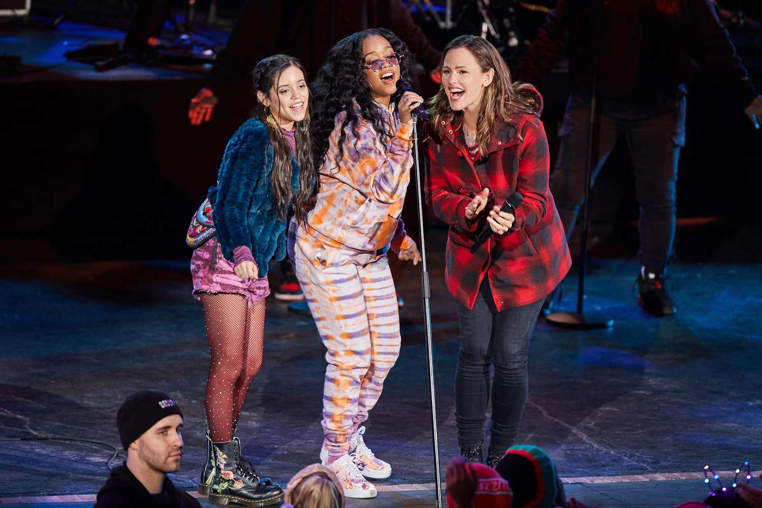 Allison and Katie on stage with H.E.R at a concert. They are all singing.