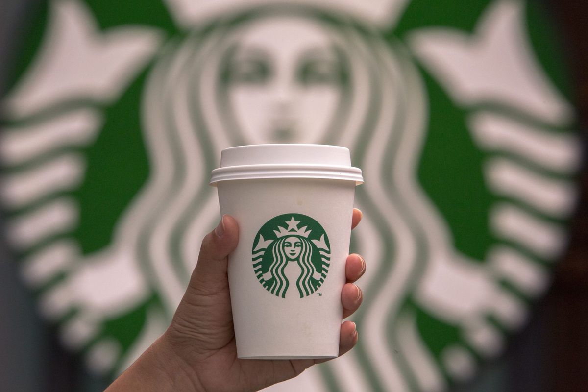 Hand holding a cup of coffee in front of Starbucks logo.