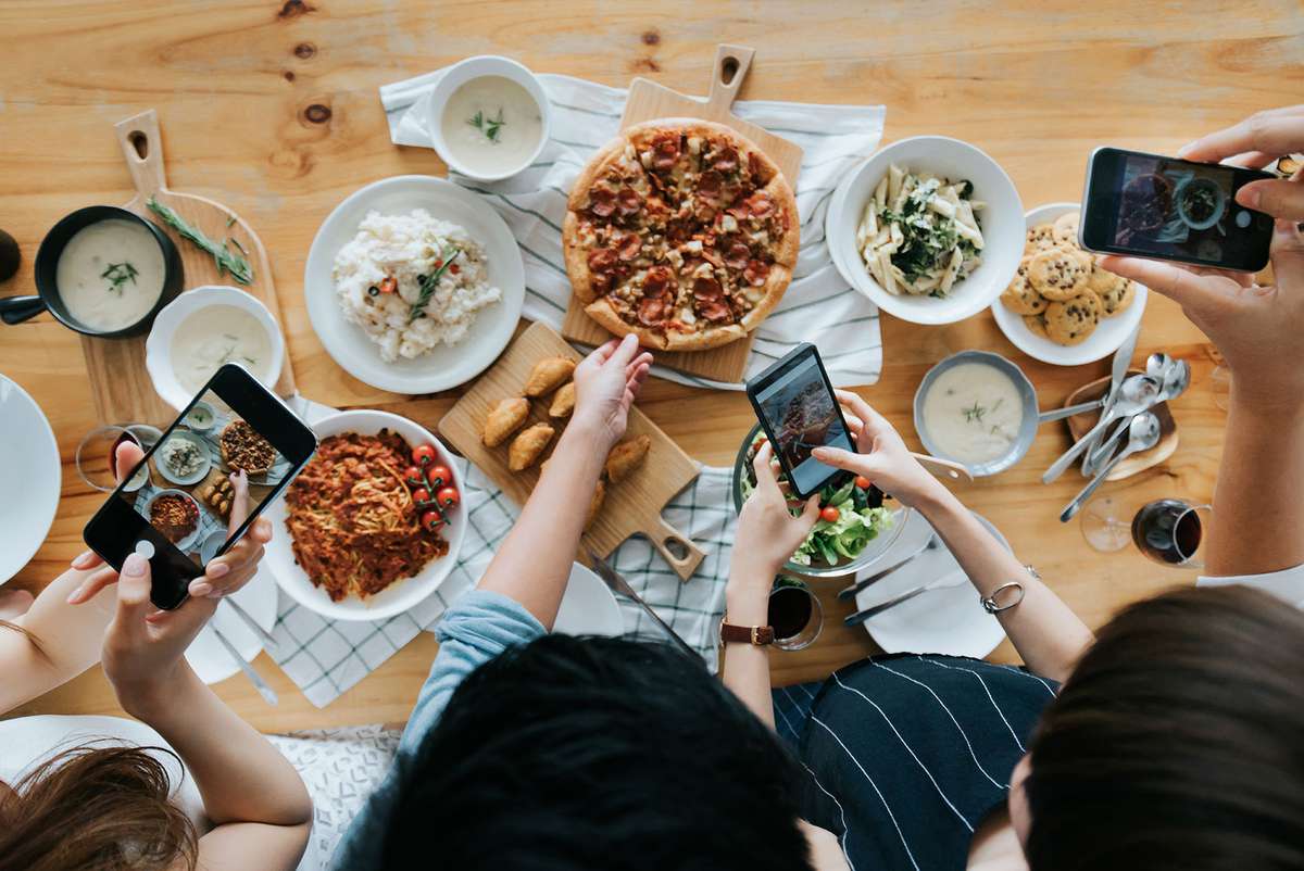 Group of friends taking pictures of food on the table with smartphones during party