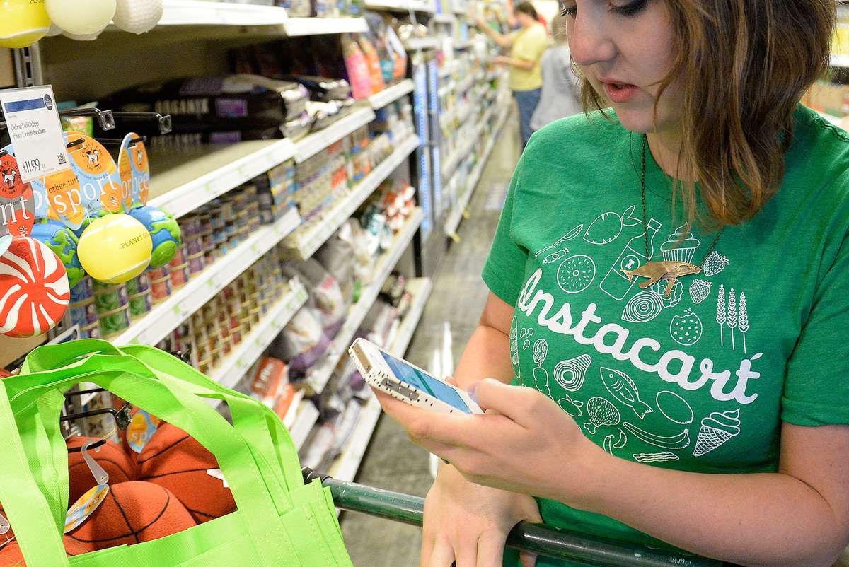 Kaitlin Myers a shopper for Instacart studies her smart phone as she shops for a customer at Whole Foods in Denver.