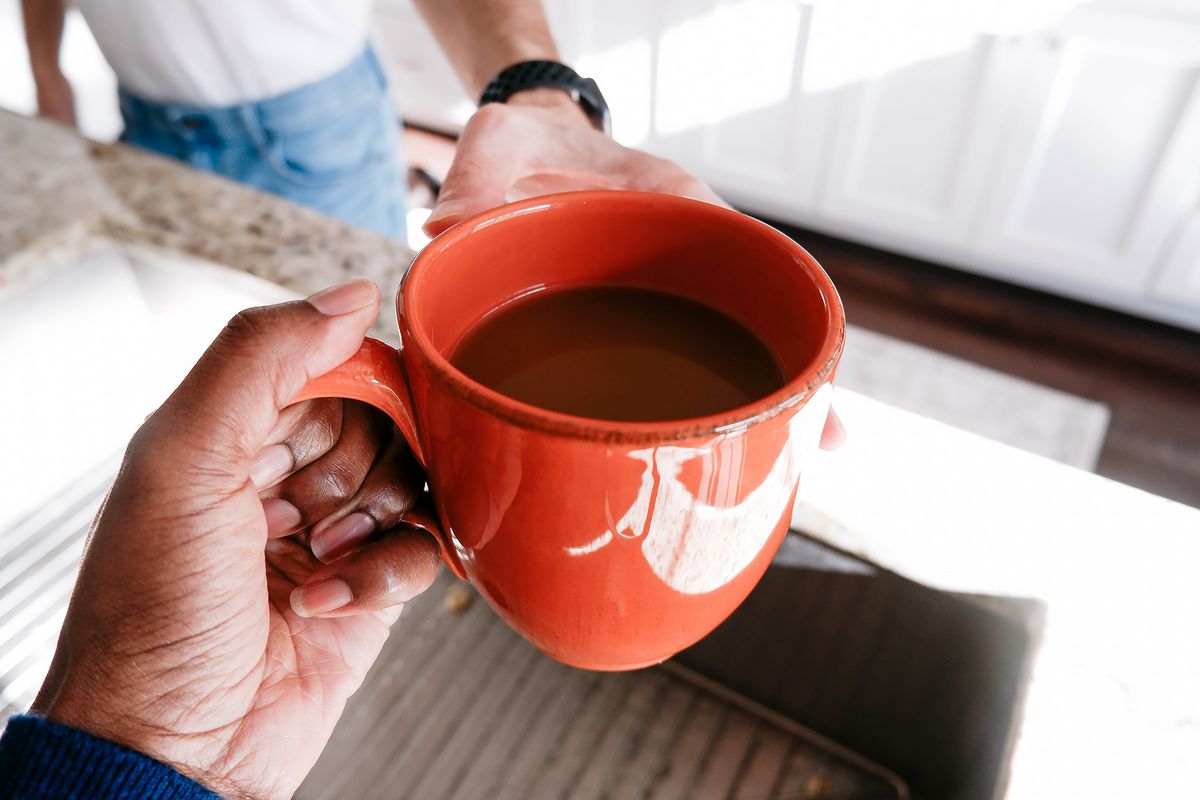 A woman hands a mug of coffee to a man