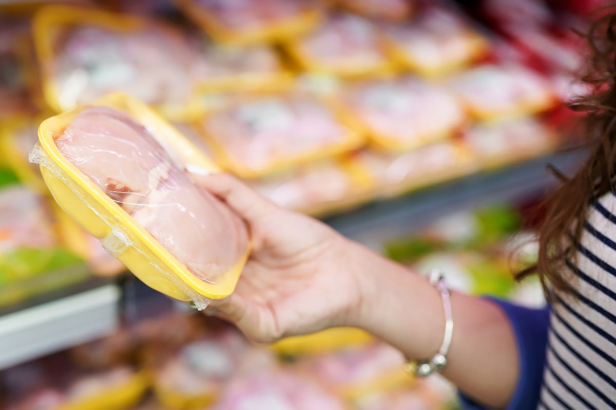 Woman choosing packed chicken meat in grocery store aisle