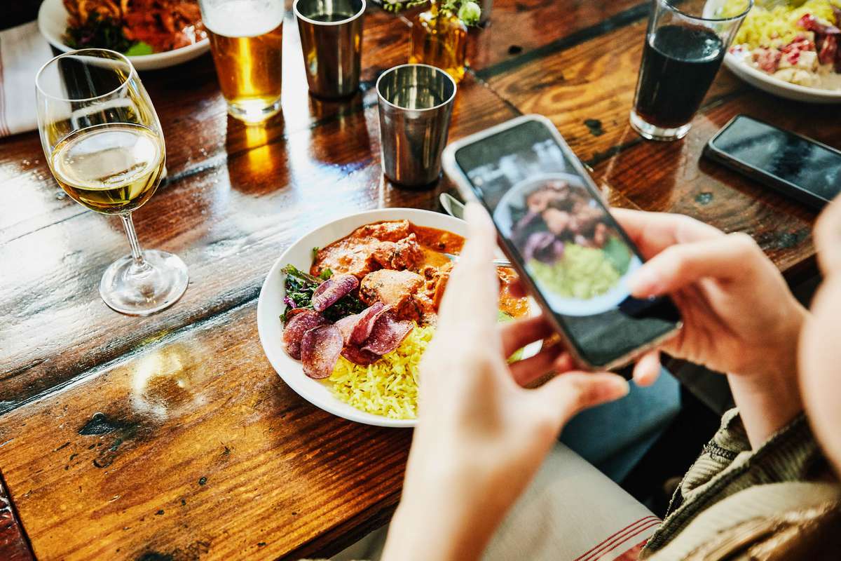 Woman taking photo of food with smartphone while having lunch with friends in restaurant