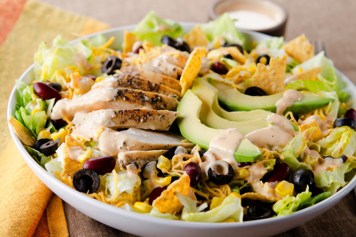 Fresh mexican-inspired salad with chicken breast, avocado, cheese, beans, iceberg lettuce, and tortilla chips
