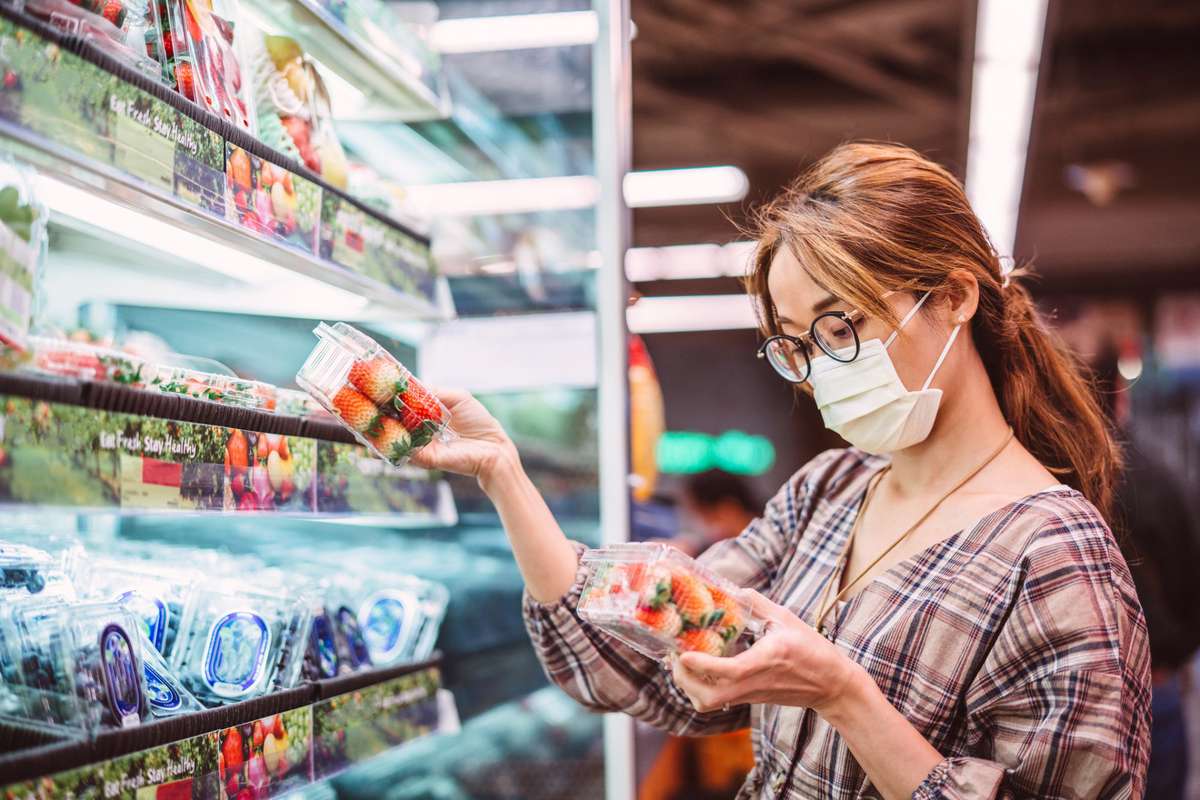 Asian woman with medical face masks doing grocery shopping for fresh fruit in supermarket