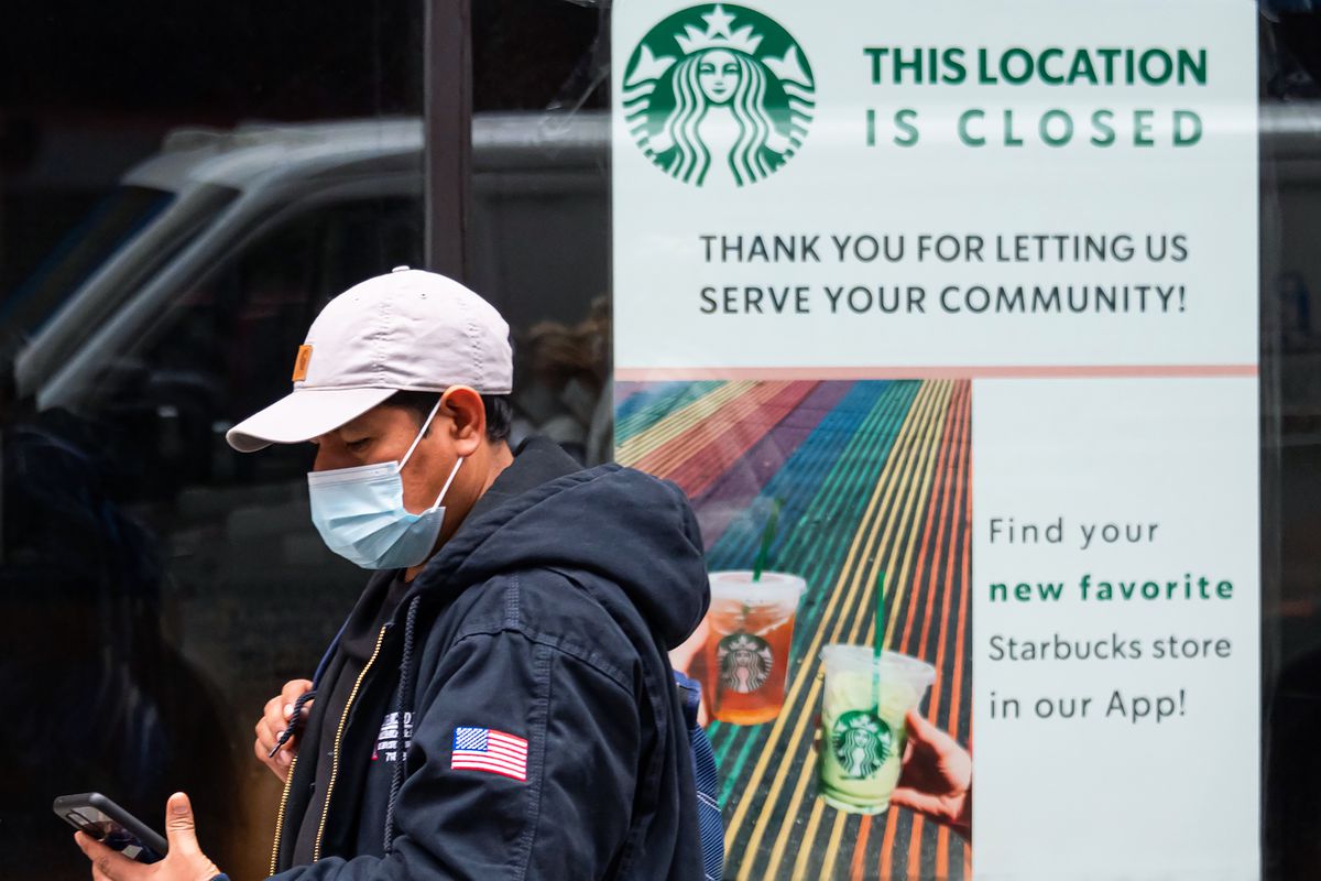 A person wearing a mask walks past a closed Starbucks location amid the COVID-19 pandemic