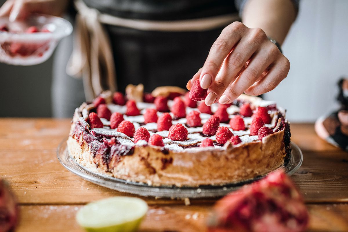 A baker tops a pie with raspberries