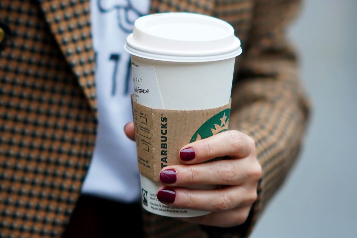 A person wearing a brown plaid jacket holds a Starbucks coffee cup