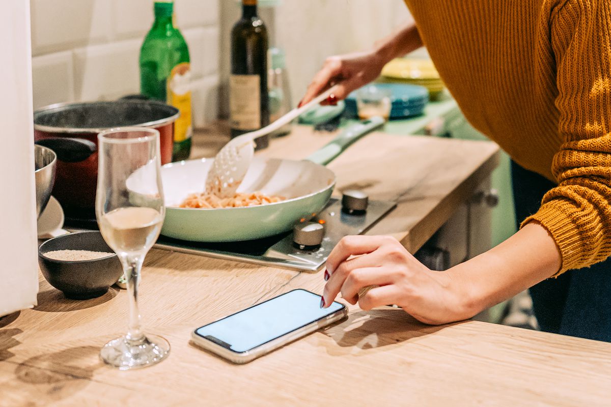 A person plays a game on their phone while cooking