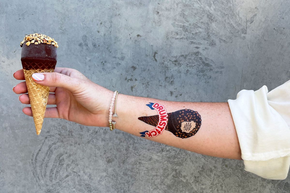 A person's forearm holding a ice cream cone and showing a tattoo of the Drumstick logo